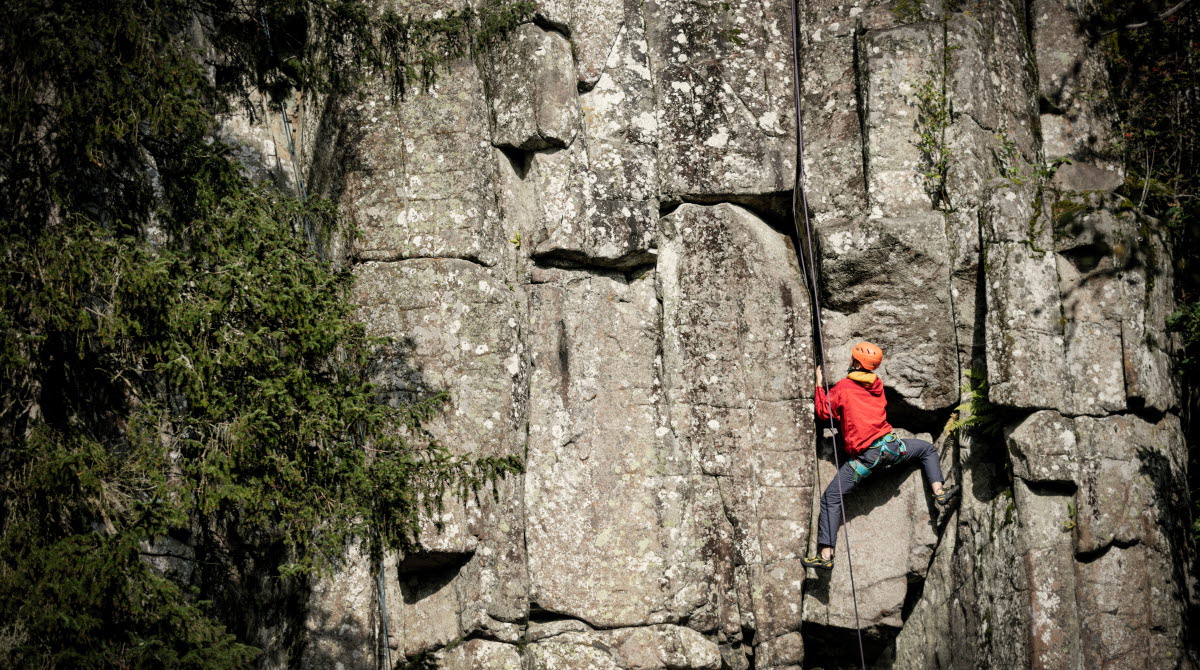 En kille i röd jacka som klättrar upp för en bergvägg. 