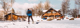 Man cross-country skiing, in the background you can see some cabins on the campsite.