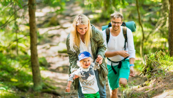 En glad familj som går uppför en backe i en grön skog.
