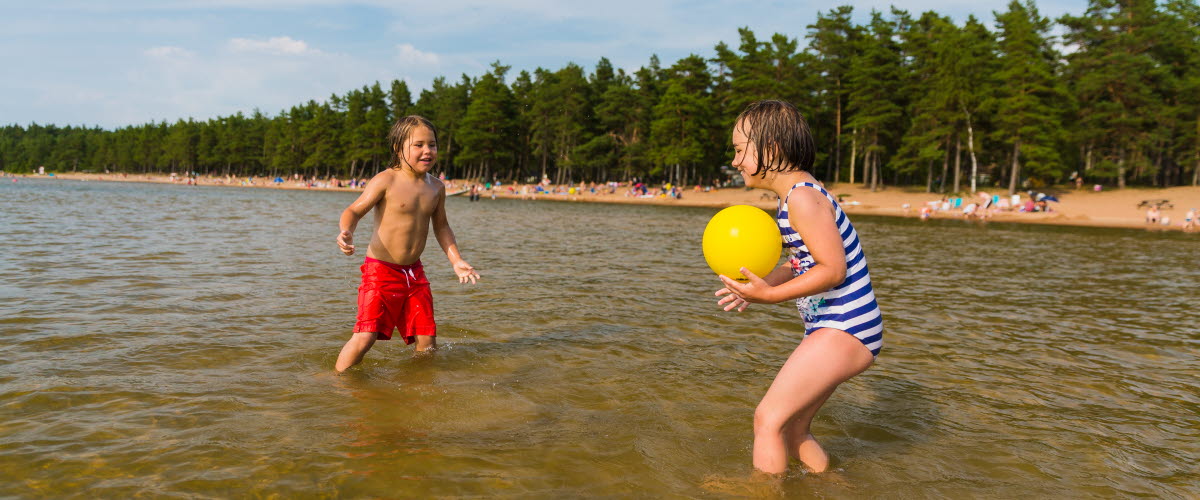 A boy and a girl throw a ball to each other in the water.