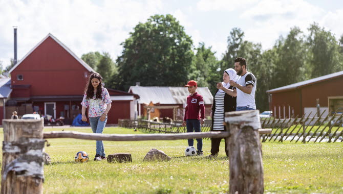 Flicka som sparkar fotboll över ett hinder. Familjen står vid sidan och hejar på.