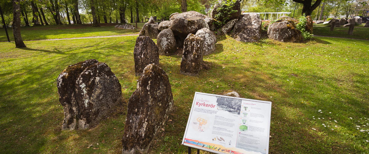 Gånggift/megalitgrav i en park. Framför gånggiften sitter en skylt med information.