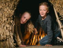 Two children peeking out from a reed hut.