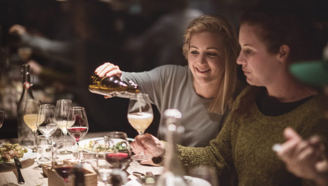 Two women having dinner. One is pouring drinks to the other one.