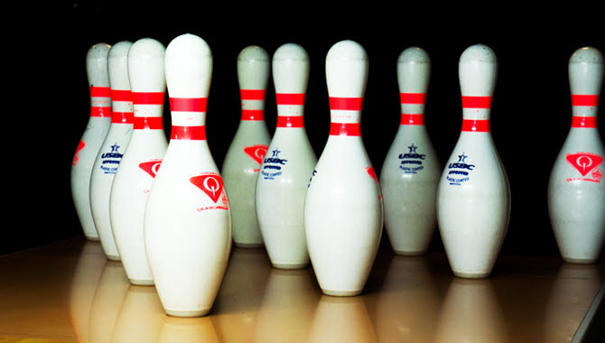 Vita bowlingkäglor med röda ränder står uppställda intill varandra redo för spel.