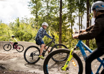 Barn och unga cyklar över grushinder i skogen. 