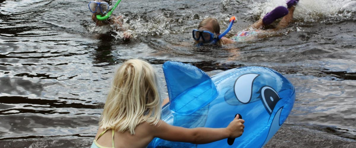 A child sitting on a blue inflatable election and two children swimming with a cyclop.