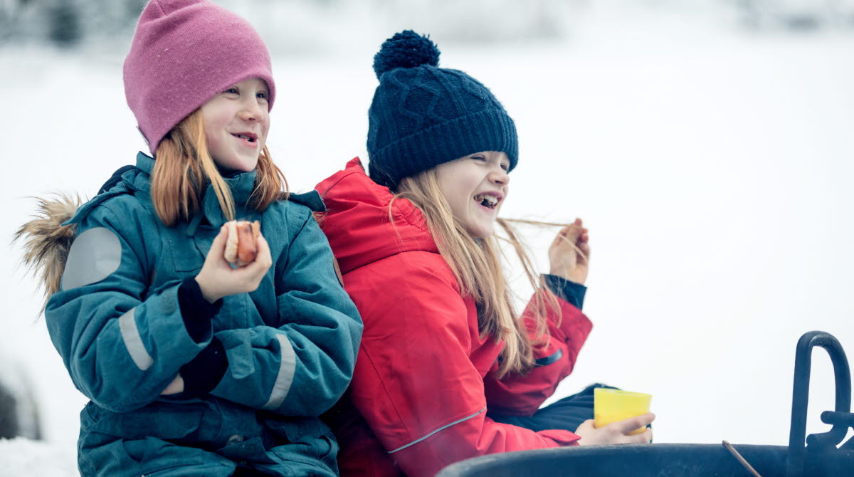 Familj som grillar i vinterlandskapet på Billingen.Två flickor äter korv och skrattar.