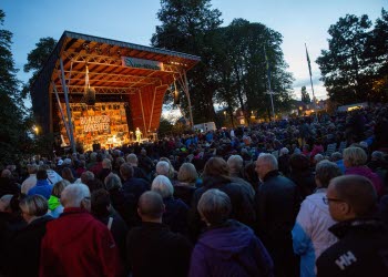 Konsert på utomhusscen i Stadsträdgården i Lidköping. Scenen lyser upp och framför står ett hav av människor.