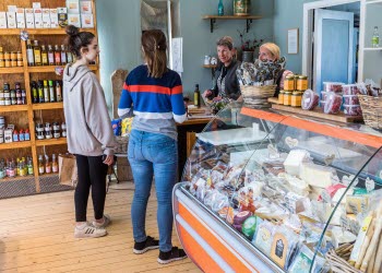 Två kvinnor står och handlar över disk i en delikatessbutik. En tredje kvinna står bakom disken och tar betalt.