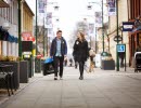 Ung man och kvinna promenerar i stadsmiljö med shoppingkassar i händerna. 