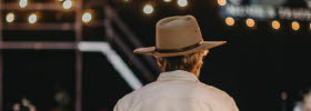 A man in a beige hat walking away from the camera.