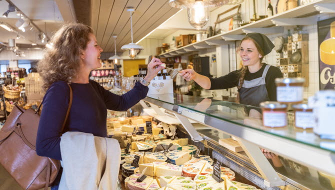Woman tasting a piece of cheese that the clerk gives her over a cheese counter.