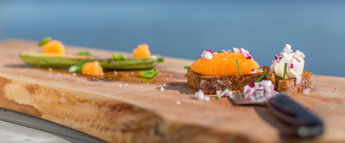 Slice of bread full of whitefish roe and chopped red onion served on a plank. In front is a knife.