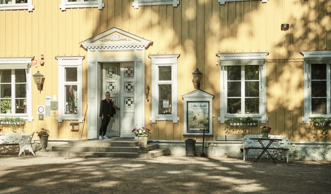 En kvinna är på väg in i ett stort vackert gult hus med vita trädetaljer. 