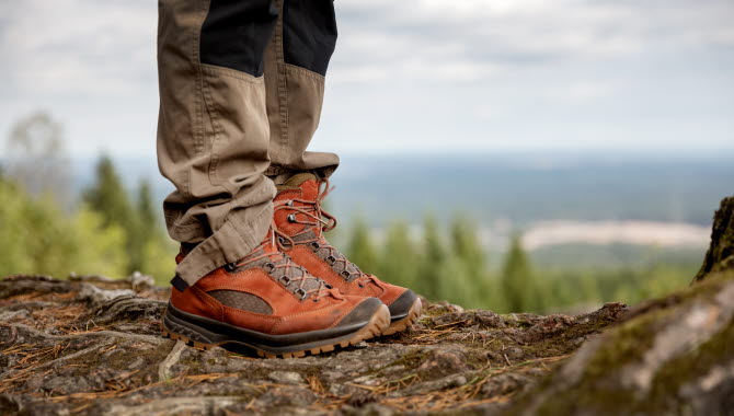 Ben i röda skor ståendes på en klippa med utsikt över skog och vidder