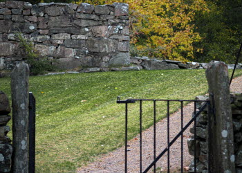 En grind och en grusgång som leder upp till en stenmur som är en del av en kyrkoruin