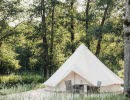 The exterior of a white glamping tent with a trolley outside. Trees and green.