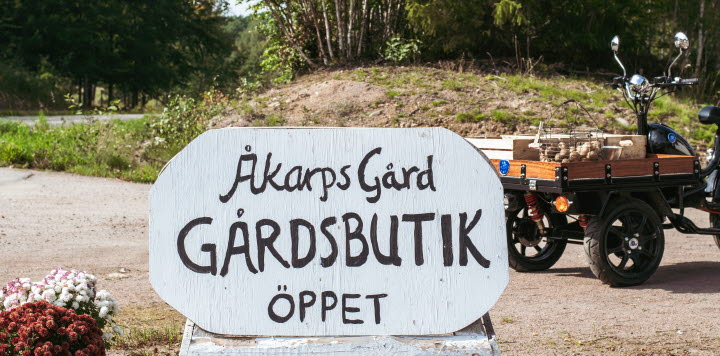 Vit skylt där det står åkarps gård gårdsbutik öppet. 