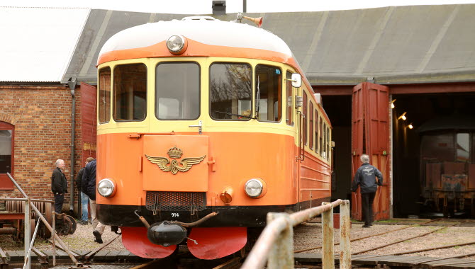 En orange tågvagn från 1900-talets första hälft rullar ut ur ett lokstall.