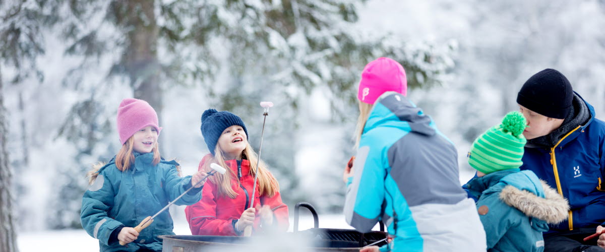 Familj sitter och grillar över öppen eld på Billingen i Skövde.