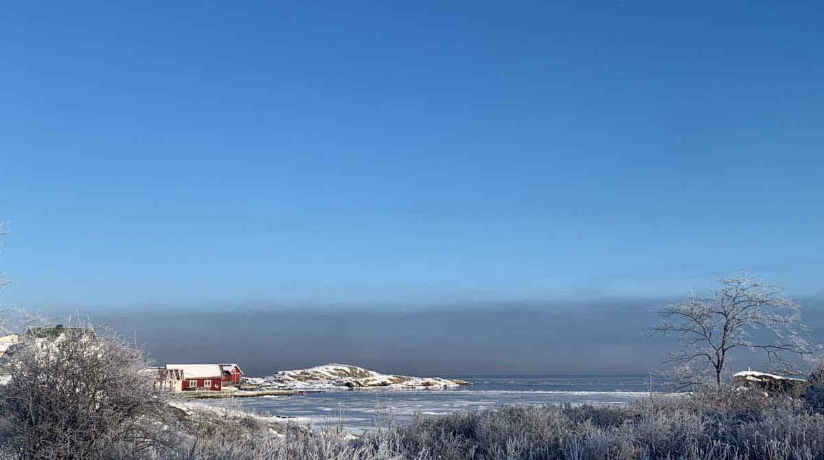 Vintrigt landskap med snö och vy ut över havet med små röda hus.