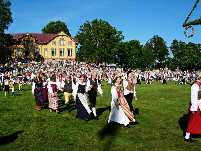Folkdansare i folkdräkt vid midsommarstången på Nääs