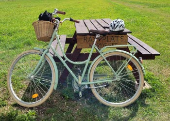 En grön cykel står lutad mot ett picknickbord. På bordet sitter en skylt med texten "Rastplats nybygget".