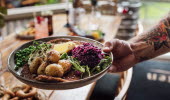 A hand with a tattoo is holding a plate with food. 