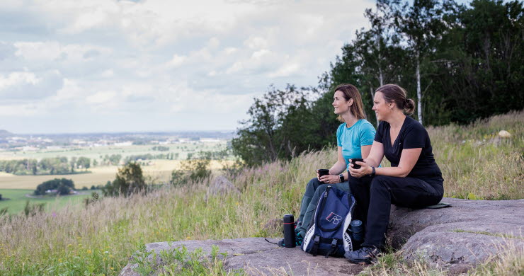 Två kvinnor som sitter på en sten och fikar och tittar på utsikten.