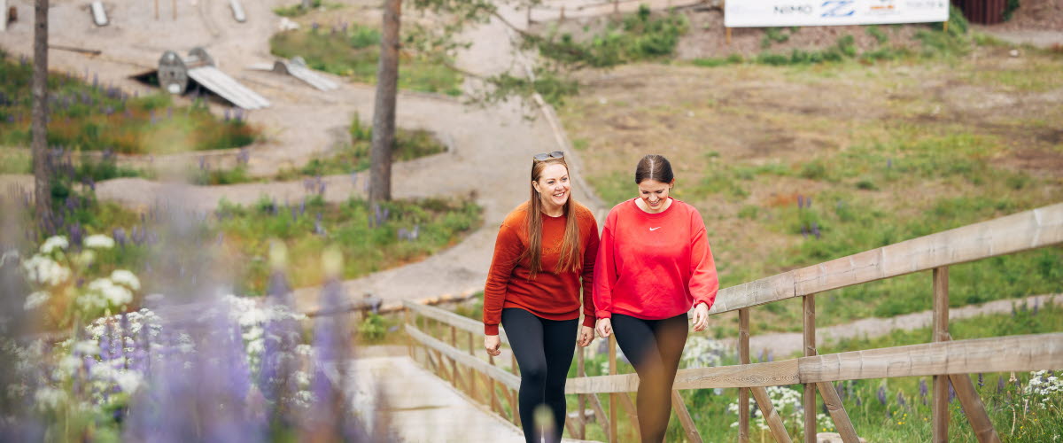 två kvinnor går uppför en motionstrappa, i bakgrunden syns delar av en bikepark