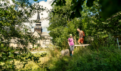 Man och kvinna som vandrar i gröngräset med Varnhems klosterkyrka i bakgrunden.