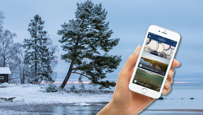 En hand som håller i en smart phone monterad på en bild över en istäckt vik.