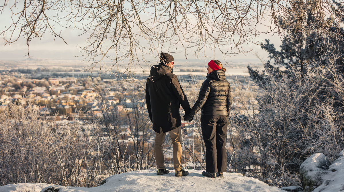 Man and woman in winter clothes peeking at the view of the city. Snowy and frosty landscape