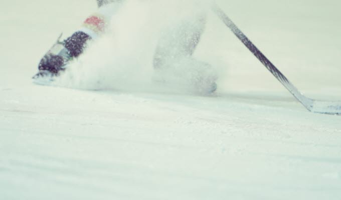 En bild på underkroppen av en person på is som bromsar med skridskorna så att det skvätter is