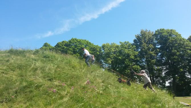Tre personer släpar ett undersökningsinstrument upp för en gravhög som de utför en markradarskanning av.
