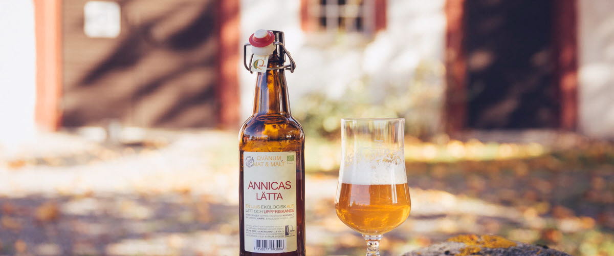 A product image of a beer and a poured glass in front of a well-kept barn.