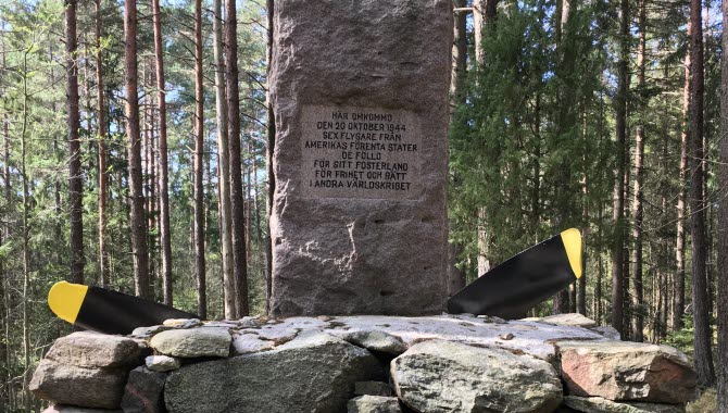 Infosten i skogen med ett stenblock.