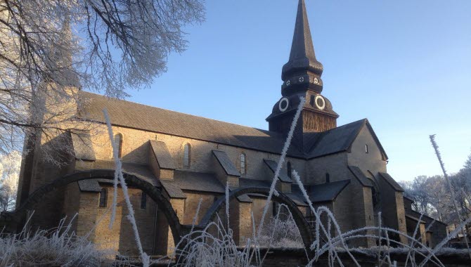 En stor grå stenkyrka med ett tjärat torn. I förgrunden syns två stenbågar från ett gammalt kloster och frostiga grässtrån.