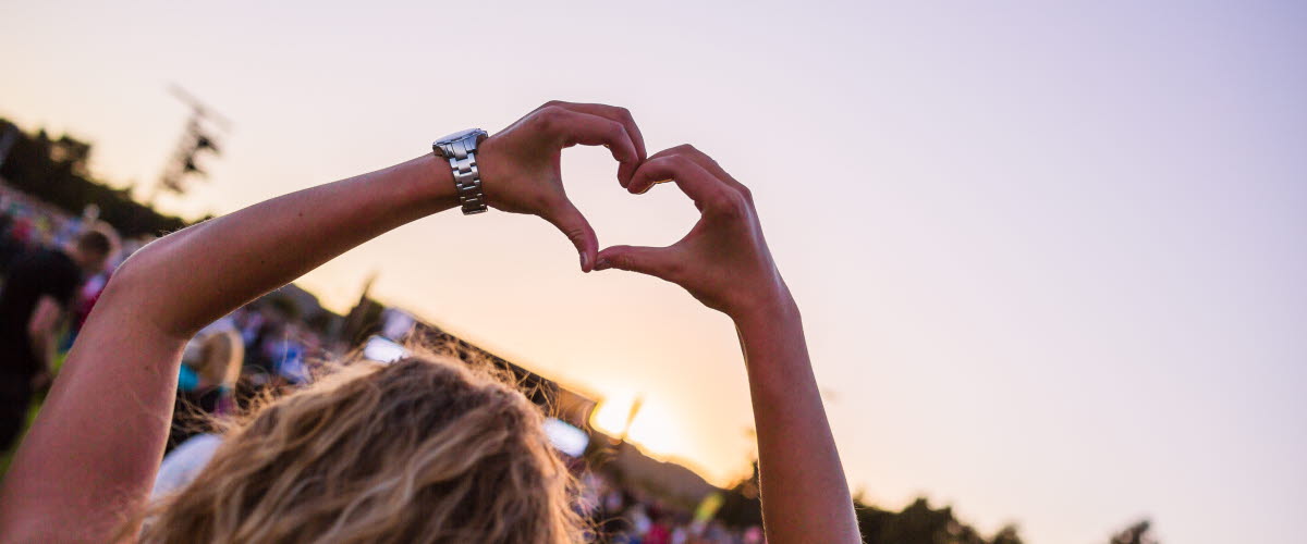 En kvinnlig åskådare på en konsert sträcker upp sina armar i luften och bildar ett hjärta med sina händer.