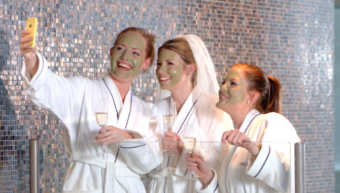 Tre tjejer poserar glatt för ett kort inne på spa-avdelningen på Strömstad Spa. De har gröna ansiktsmasker, är iförda badrockar och håller varsitt champagneglas.