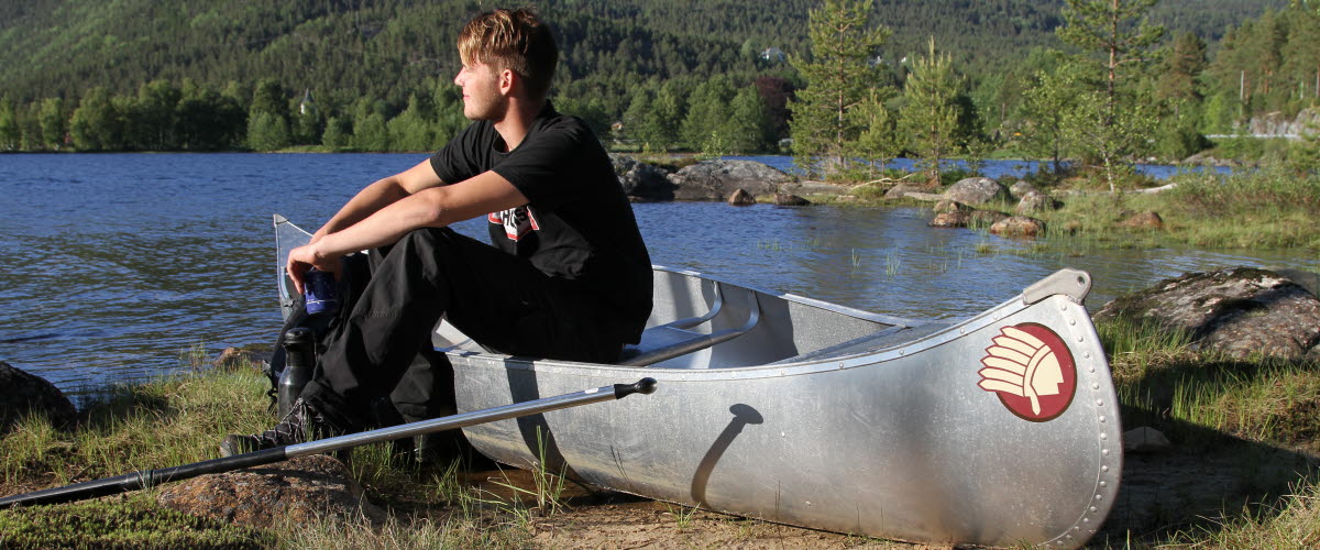 En ung man sittande på en kanot på stranden och ser nöjd ut