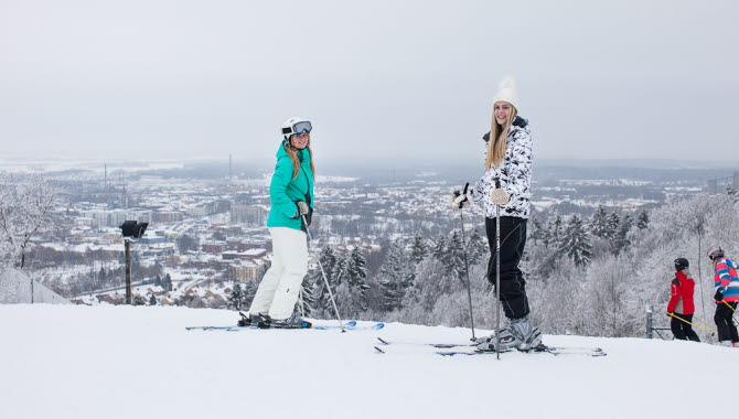 Two girls standing in the top of a ski slope with skis on their feet and a magical view. 