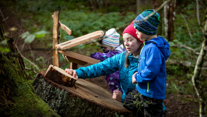 En kvinna med två barn utforskar stockar i naturen.