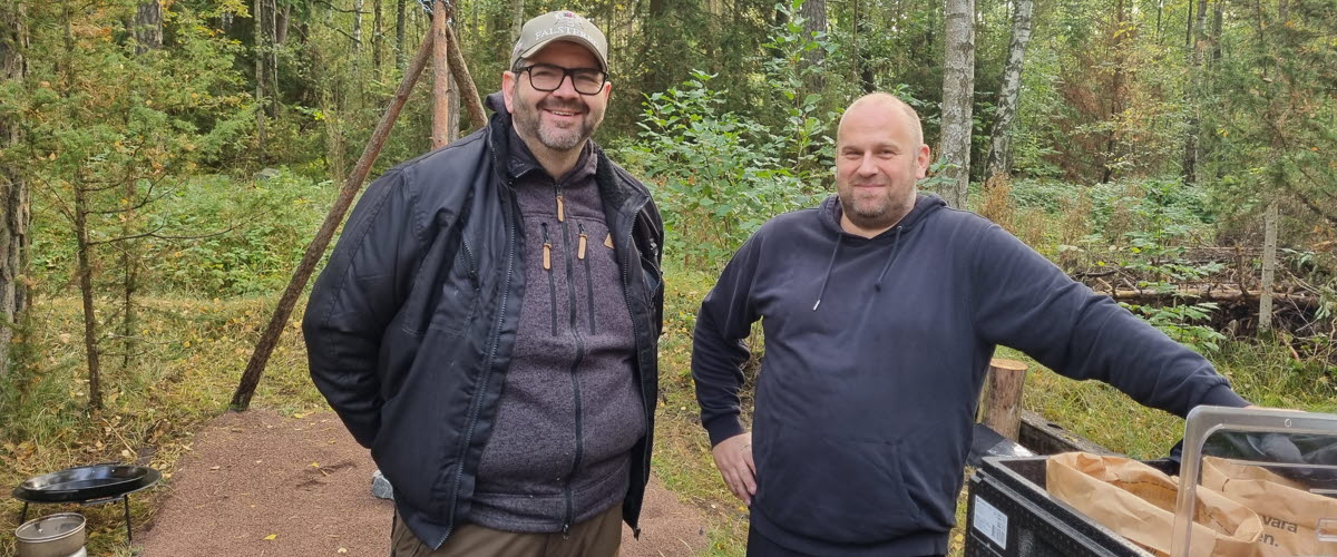 Två män som står framför en skog. 