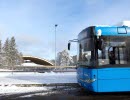 Framdelen av en blå bussar, i bakgrunden ser du snö och skog, en människa går ut ur bilden till vänster.