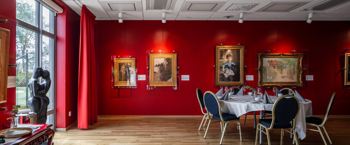 A room with red walls and big windows. Valuable paintings are hanging on the walls. A table and chairs on the floor.