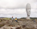 Two women sit on a rock in a sculpture park.