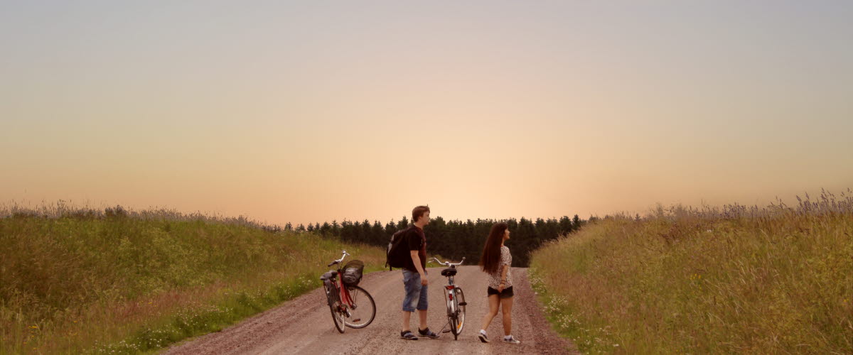 Två personer står intill sina cyklar på en grusväg i solnedgången.