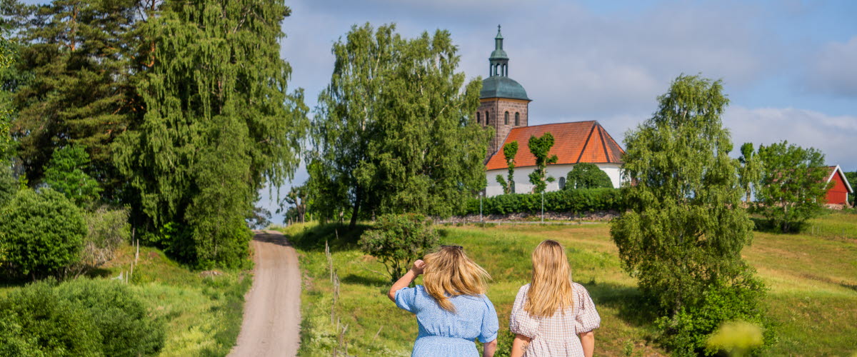 Två kvinnor klädda i sommarklänningar som tittar ut på en äng och en kyrka.
